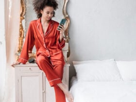 Biracial woman wearing red silk pajamas in a bedroom while holding her phone